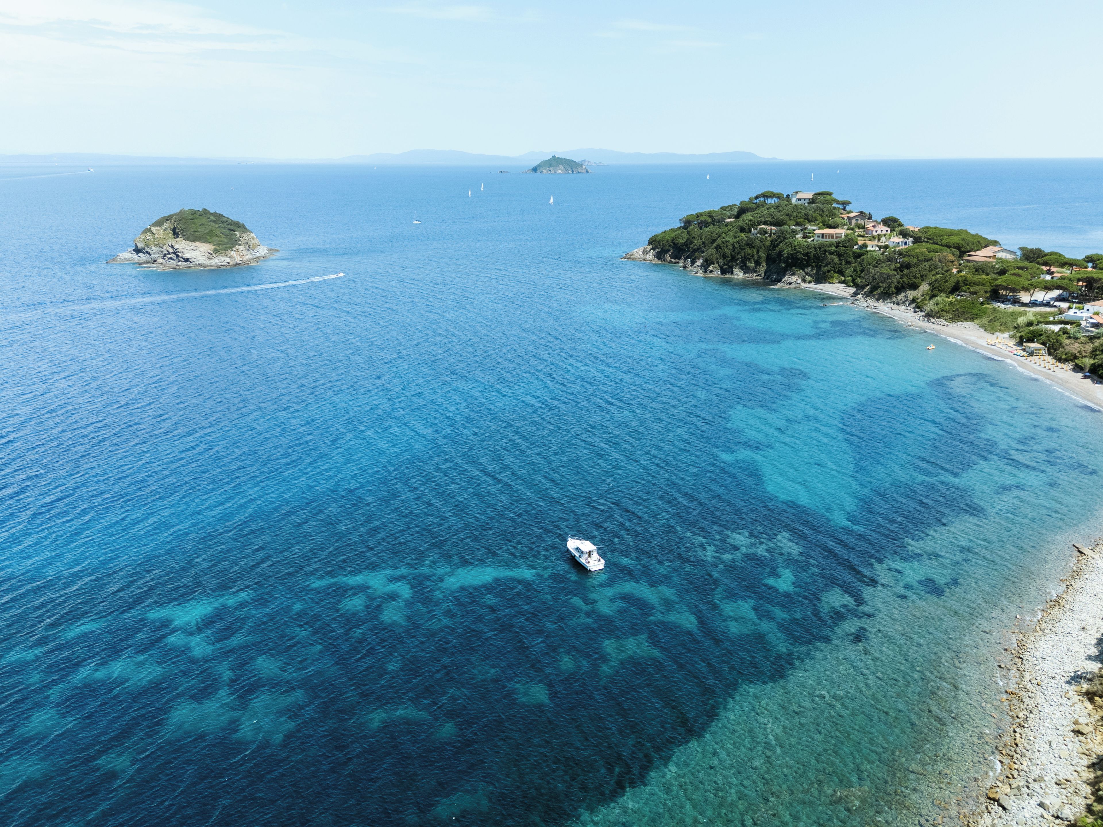 A coastal landscape with clear blue waters, a small island, and a beach with buildings.