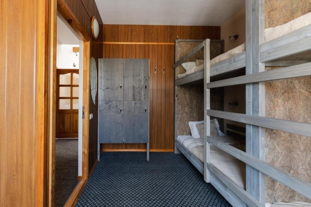 Une chambre avec des lits superposés, une armoire et une porte qui donne sur une autre pièce.