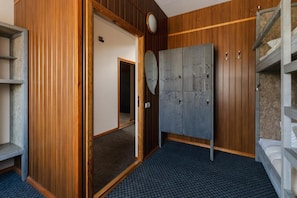A room with a wooden wardrobe, a bed with a white mattress, and a blue patterned floor. - Hang the Hat (Valmiera)