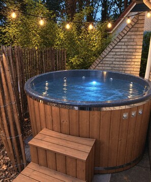 A hot tub with a wooden exterior, surrounded by a wooden deck and a bamboo fence. - Gemütliches Ferienhaus für 2-6 Personen mit privater Hottub in schönen Lochem (Lochem)