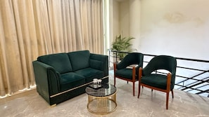 Una sala de estar moderna con un sofá verde oscuro, dos sillones a juego y una mesa de centro con detalles dorados.