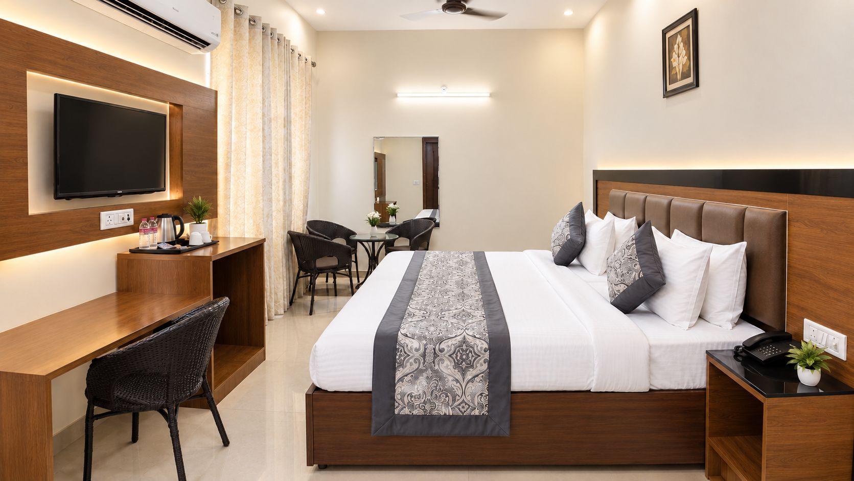 Habitación de hotel con cama, escritorio, silla, televisión y una pequeña mesa con una planta.