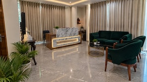 Una sala moderna con un mostrador de recepción de mármol, sofás de terciopelo verde y una mesa de centro redonda.