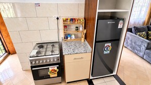 A compact kitchen with a gas stove, oven, and a black refrigerator. - 2 Bedroom Bungalow in Nyali (Mombasa)