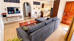 A living room with a grey sofa, a wooden coffee table, and a TV mounted on the wall. - 2 Bedroom Bungalow in Nyali (Mombasa)