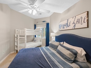 Ein Schlafzimmer mit Etagenbetten, einem Bett mit blauer Kopfteil, einem Deckenventilator und einem Wandschild mit der Aufschrift 'No Wake Zone'.
