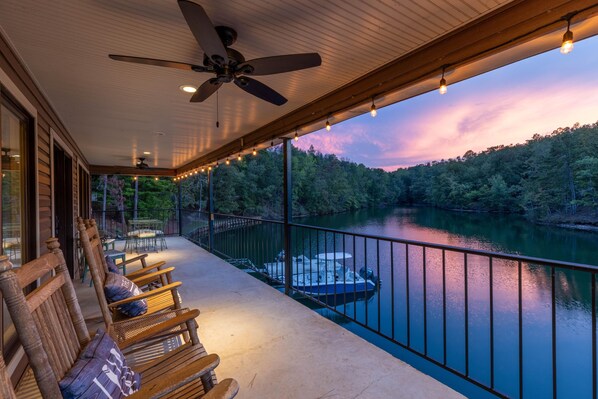 A covered outdoor area with a view of a river, wooden seating, and a boat docked on the water.