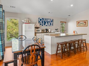 A kitchen with a central island, wooden chairs, a dining table, and a view of trees through the window. - 2 houses sit on 1350ft Peninsula-Sleeps 18-Waterslide. Green light. Fish Feeder. (Dadeville)
