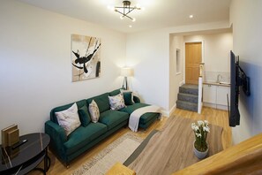 Ein modernes Wohnzimmer mit einem grünen Sofa, einem Gemälde, einer Lampe und einer Treppe, die zu einer Küche führt.