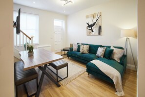 A modern living room with a wooden dining table, a green sofa, and a painting on the wall. - Host Stay - Temperance Mews (Saltburn-by-the-Sea)