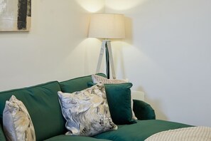 A green sofa with multiple cushions, a floor lamp, and a painting on the wall. - Host Stay - Temperance Mews (Saltburn-by-the-Sea)