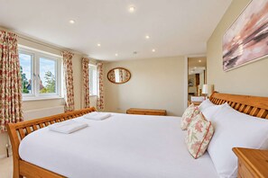 A bedroom with a wooden bed, white bedding, floral curtains, a round mirror, and a painting on the wall. - Host Stay - Yeoman s House (Canterbury)