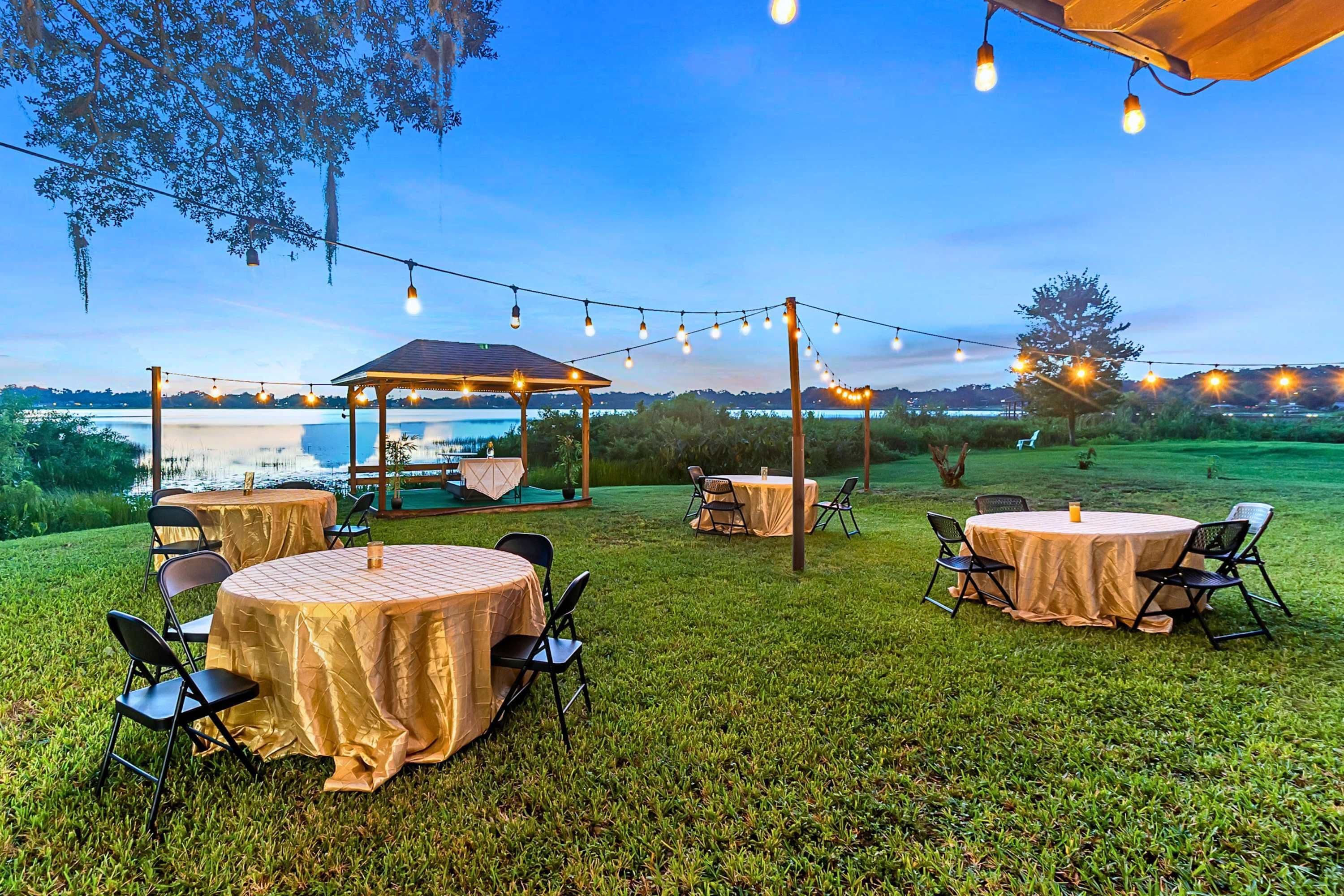 An outdoor seating area with round tables and chairs, string lights, and a gazebo overlooking a body of water.