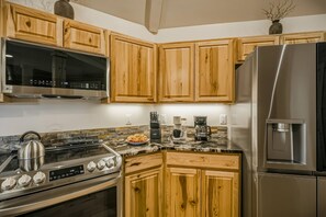 Een keuken met houten kastjes, een roestvrijstalen koelkast, een magnetron, een fornuis en een koffiezetapparaat.