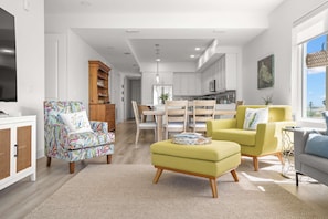 Ein modernes Wohnzimmer mit Flachbildfernseher, einem Essbereich mit Holztisch und Stühlen sowie einer Küche im Hintergrund.