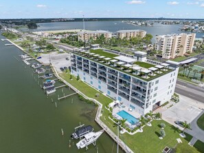 Ein mehrstöckiges Hotel mit Pool auf dem Dach, in der Nähe eines Hafens mit vor Anker liegenden Booten.