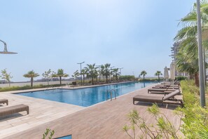 A swimming pool with lounge chairs and palm trees. - Stayshort - Cozy Studio in Damac Hills 1 for 2 With Pool Access (Dubai)