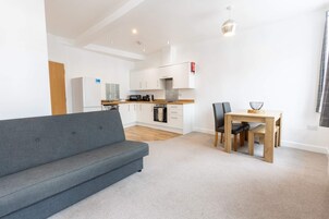 En moderne lejlighed med en grå sofa, et spisebord med stole, et køkken og en lille opholdsstue.