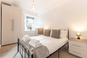 Un dormitorio moderno con cama, mesitas de noche, ventana y armario.