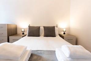 Habitación de hotel con cama, dos mesitas de noche, dos lámparas, un armario de madera y dos toallas.
