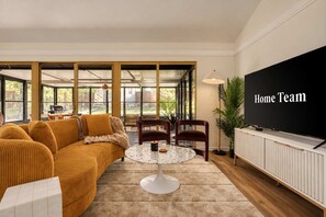 A living room with a sofa, chairs, a coffee table, a TV, and a large window. - Southbound Social Pool Patio Games Movies (Austin)