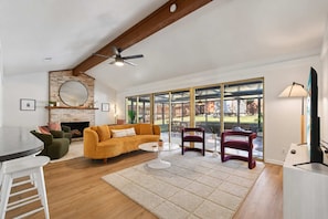 A spacious living room with a fireplace, a large window, and a ceiling fan. - Southbound Social Pool Patio Games Movies (Austin)