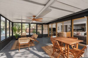 A spacious room with a large table and chairs, a ceiling fan, and large windows offering views of the outdoors. - Southbound Social Pool Patio Games Movies (Austin)