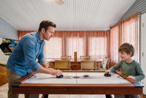 Ein Mann und ein Kind spielen Ruckel, in einem Raum mit Esstisch, Stühlen, Holzboden und Deckenventilator.