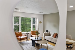 A modern living room with a sofa, armchairs, a coffee table, and a lamp. - Your Poconos Escape Game Room Firepit Grill (Tobyhanna)