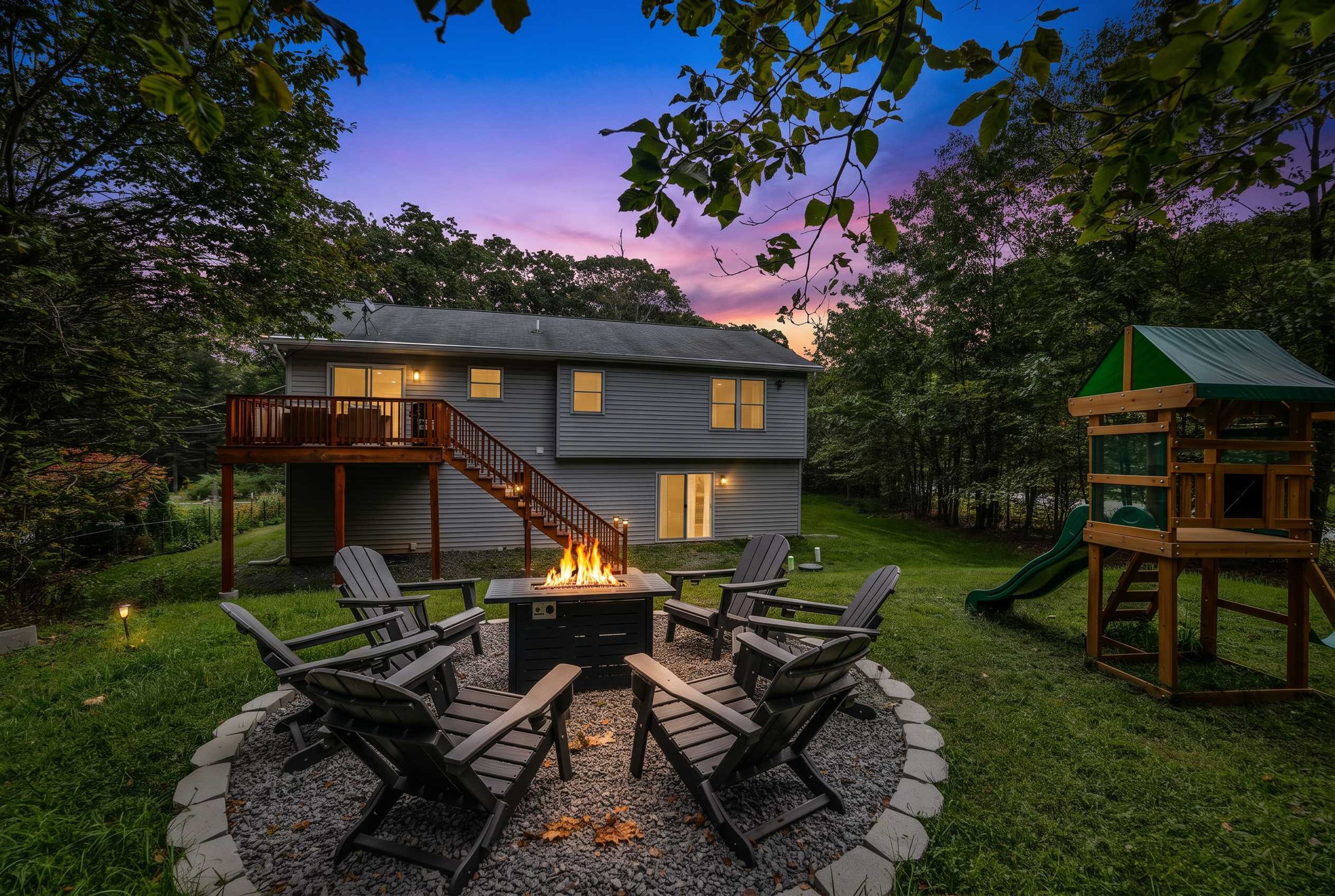A house with a fire pit and outdoor seating, surrounded by a deck and a slide.