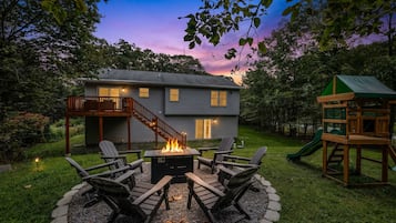 A house with a fire pit and outdoor seating, surrounded by a deck and a slide.