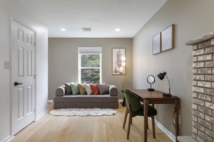 Una habitación con sofá, escritorio, silla, alfombra y pared de ladrillo.