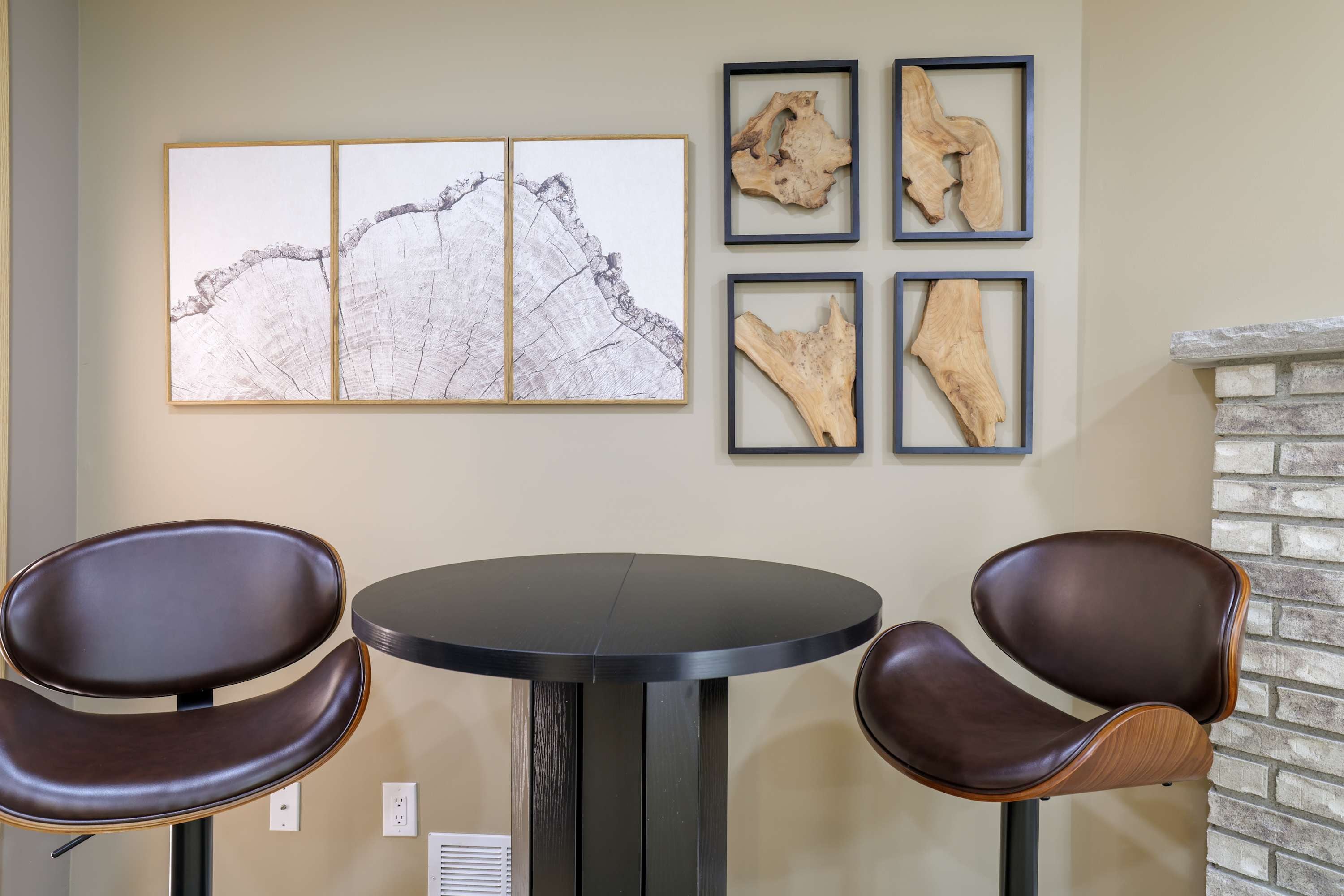 A room with a round table, two leather chairs, a fireplace, and four framed artworks on the wall.
