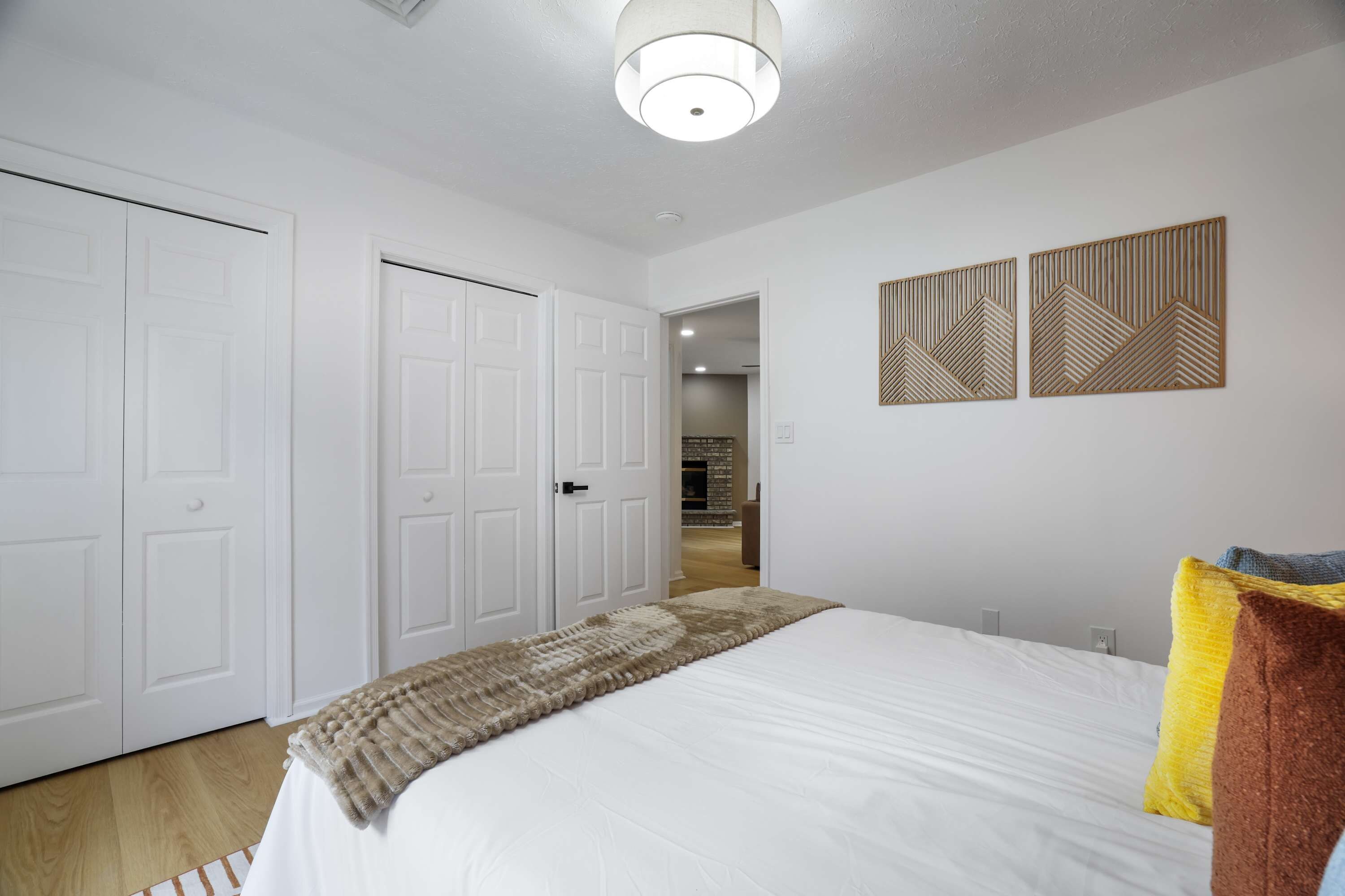 A bedroom with a bed, white walls, a ceiling light, and two wooden wall art pieces.