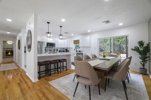 A modern kitchen with white cabinets, a central island with bar stools, and a dining area with a large table and chairs. - Your Poconos Escape Game Room Firepit Grill (Tobyhanna)