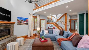 A spacious living room with a fireplace, a large sofa, a coffee table, and a staircase leading to an upper level.