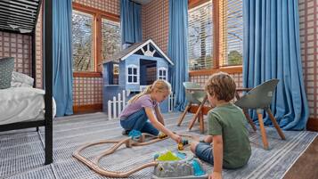 A room with a bed, a play area with toys, and a window with curtains.