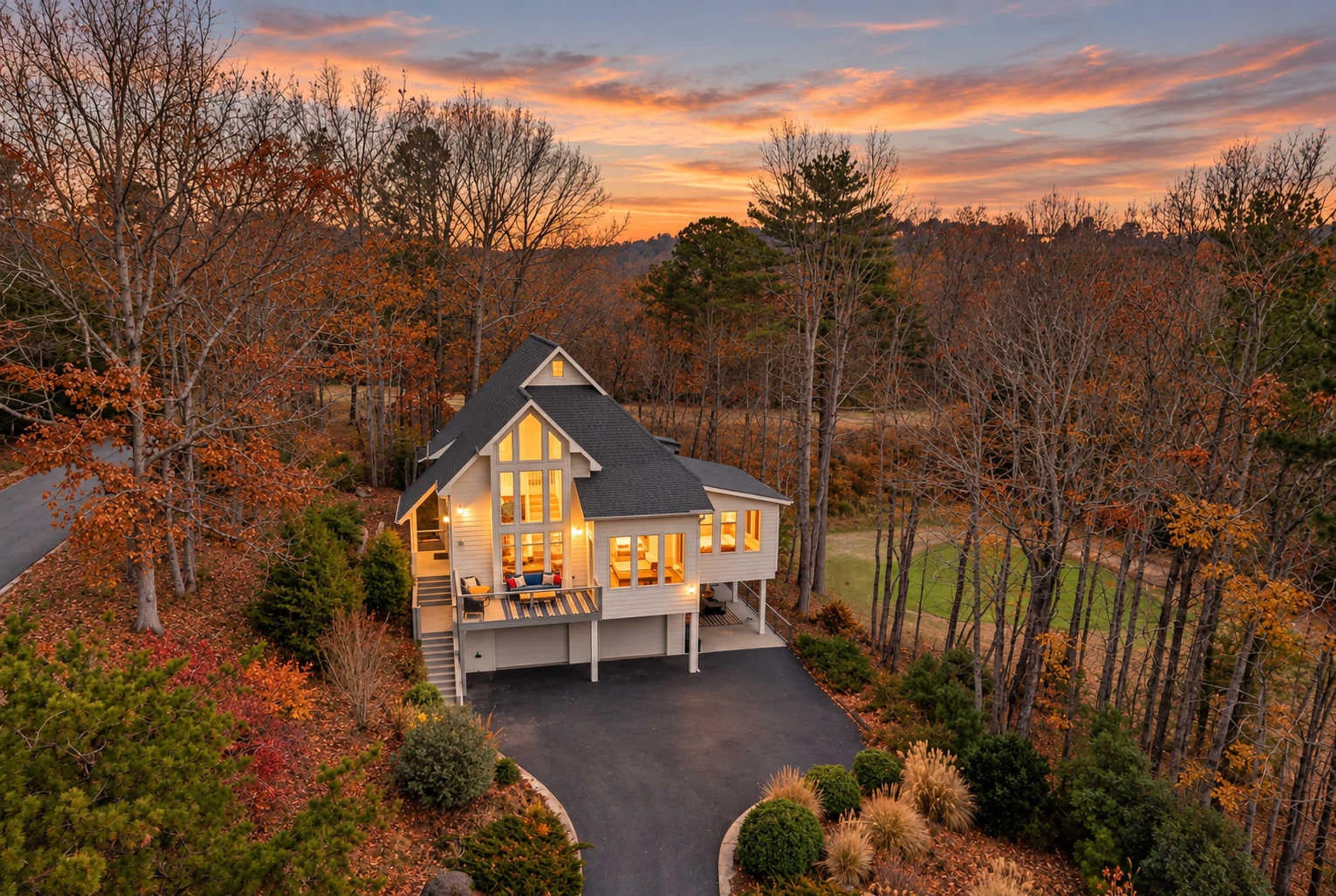A two-story house with a large porch and multiple windows, surrounded by trees and a driveway.