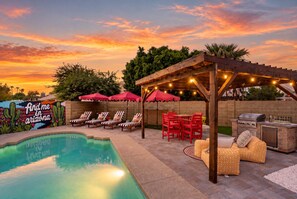 Ein Poolbereich mit Grillmöglichkeit, Liegestühlen und einer Pergola mit Lichterketten.
