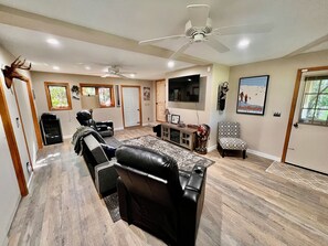 A spacious living room with a large flat-screen TV, leather sofas, a patterned rug, and a ceiling fan. - Mountainview Manor with VIEWS GALORE in Beech Mountain close to the ski slopes (Beech Mountain)
