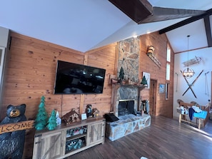 Interior acogedor de una cabaña con chimenea, paredes de madera, un televisor montado y una decoración con un oso.