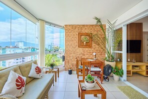 A balcony with a sofa, dining table, chairs, and potted plants. - Apartment in Condominium Itagua Viewpoint - Between Praia Grande and Tenório - 10 min walk (Ubatuba)