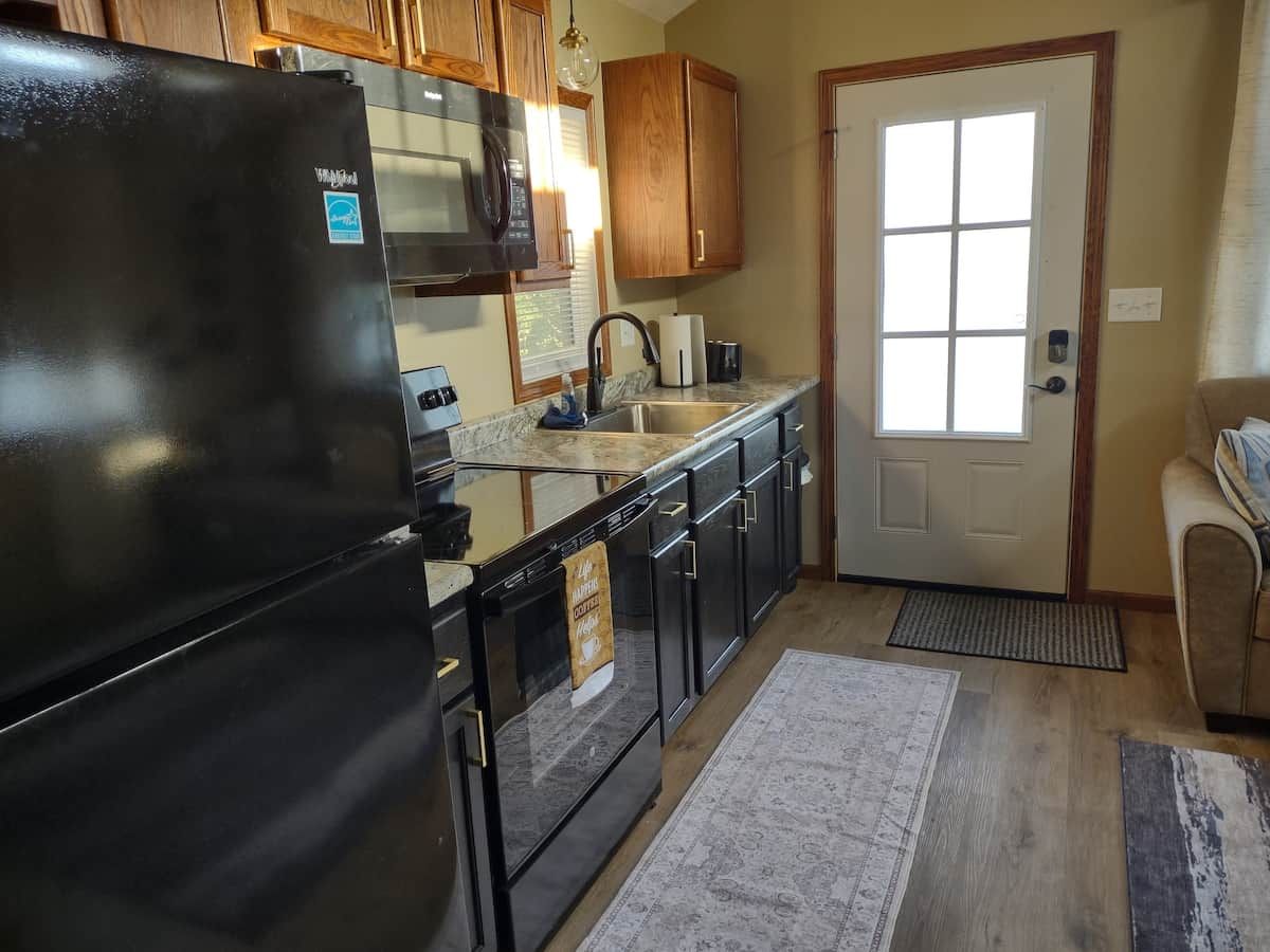 A kitchen with a black refrigerator, wooden cabinets, a stainless steel sink, and a door with a window.