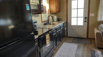 A kitchen with a black refrigerator, wooden cabinets, a stainless steel sink, and a door with a window.
