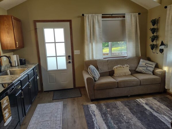 A compact living space with a kitchenette, a sofa, and a window with curtains.