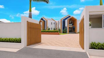 A modern residential building with a gated entrance, a well-maintained garden, and a clear sky.