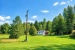 A house with a porch, surrounded by a green lawn and tall trees. - Original Camp Bungalow; 12 Acres; Trampoline (Roscoe)