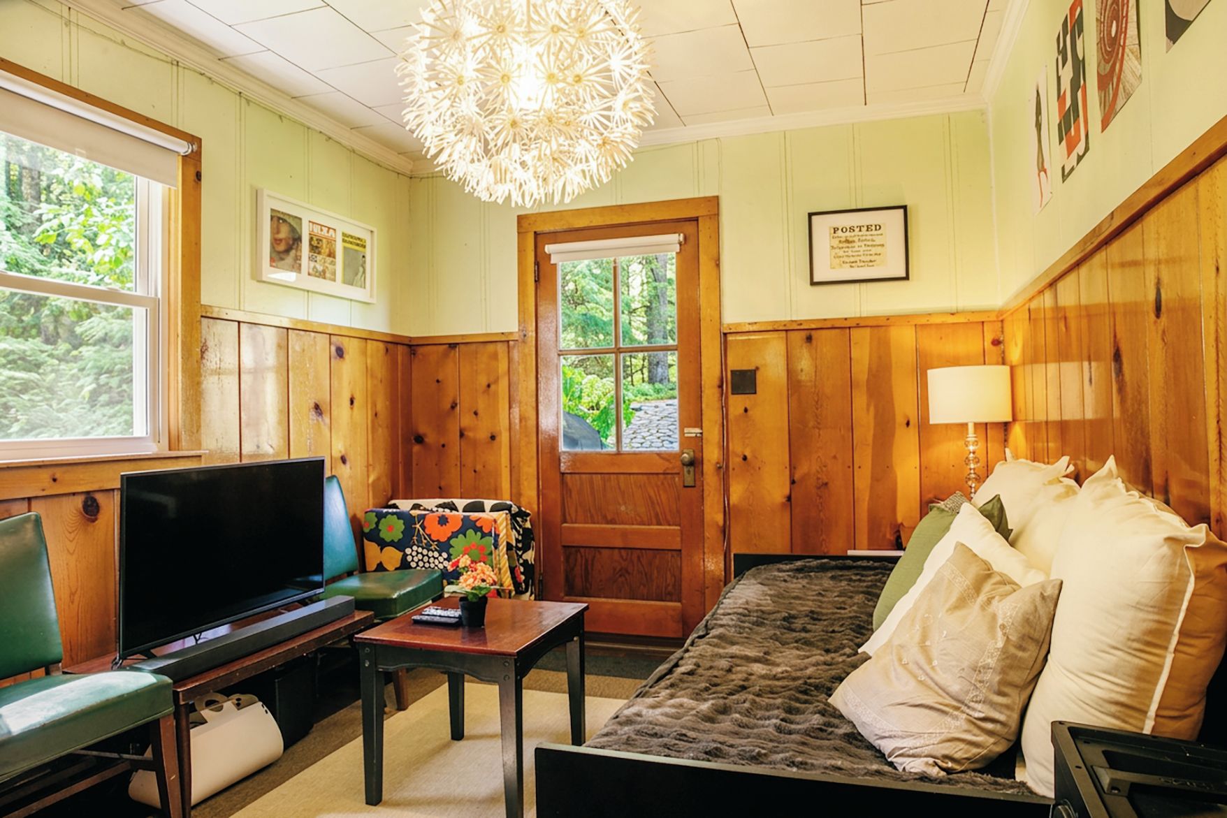 A cozy room with a television, a sofa, a table with a vase, and a door leading outside.