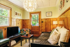 A cozy room with a television, a sofa, a table with a vase, and a door leading outside.