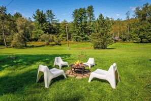 Un espace extérieur aménagé avec quatre chaises blanches disposées autour d’un foyer.